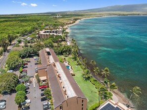 An aerial view of a coastal area with a parking lot, buildings, and a beach. - Remodeled Oceanfront 1BD with Stunning Sunset Views- Maalaea Banyans 316 (Wailuku)