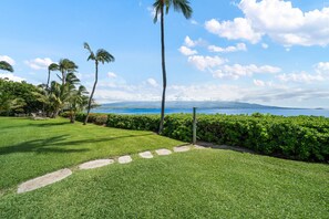 A well-maintained lawn with a stone pathway leading to a view of the ocean. - Remodeled Oceanfront 1BD with Stunning Sunset Views- Maalaea Banyans 316 (Wailuku)