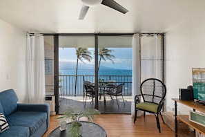 A balcony with a view of the ocean, a dining table, chairs, a sofa, and a television. - Remodeled Oceanfront 1BD with Stunning Sunset Views- Maalaea Banyans 316 (Wailuku)