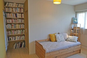 Ein Schlafzimmer mit einem hölzernen Bett, einem Bücherregal und einem Fenster mit Vorhängen.