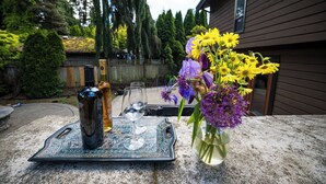 A patio with a tray holding wine bottles and glasses, a vase with flowers, and a wooden fence in the background.