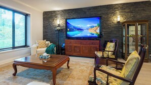A living room with a large flat-screen TV, a sofa, a coffee table, and a cabinet.