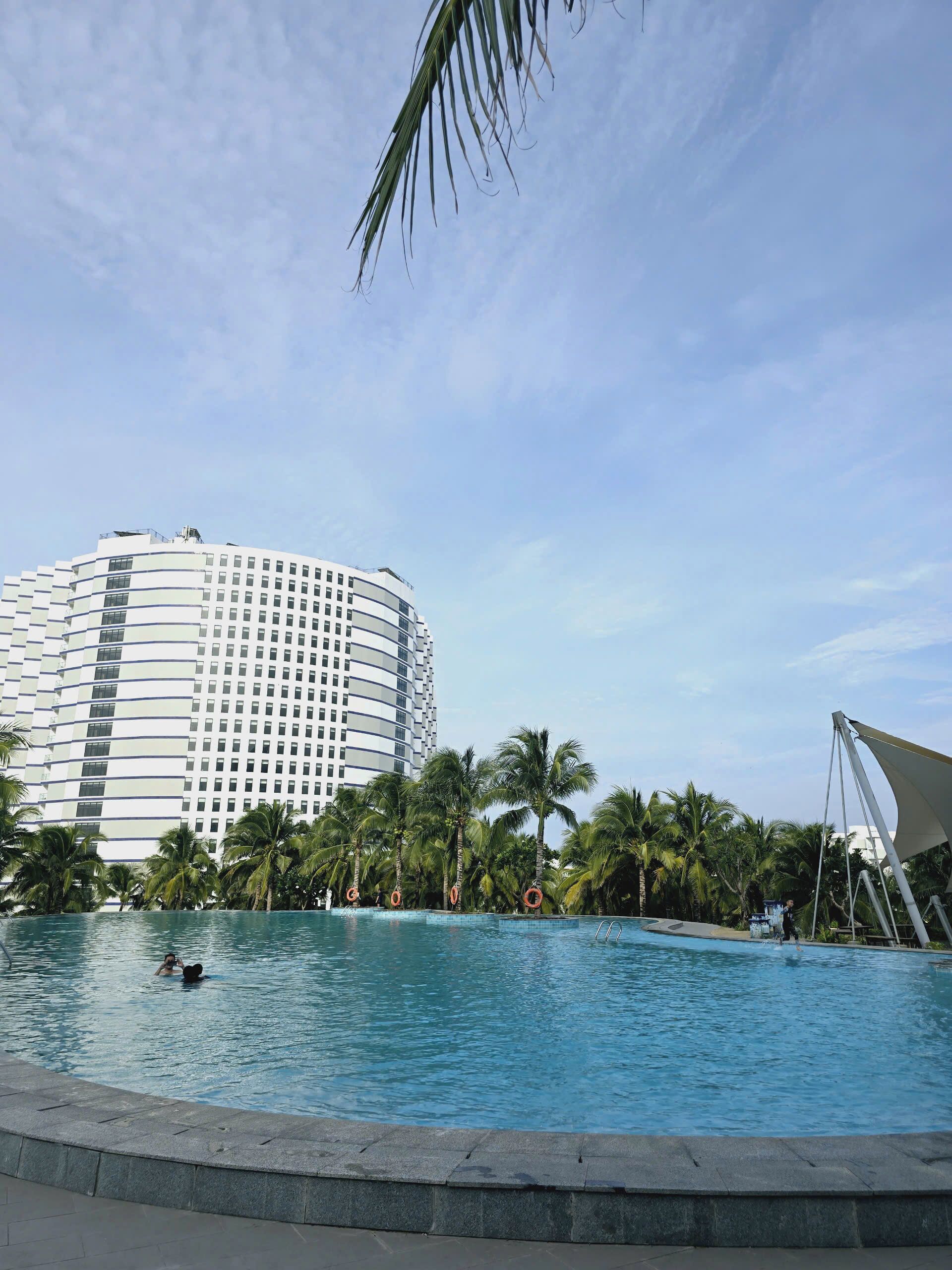 A swimming pool with palm trees and a large hotel building in the background.