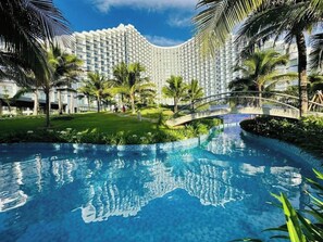 A hotel with a large pool, palm trees, and a bridge. - Arena Cam Ranh Condotel With Beachfront (Bắc Cam Ranh)