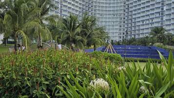 A modern hotel with a curved facade, lush greenery, and palm trees.