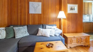 En stue med sofa, sofabord, lampe og træpaneler på væggene.