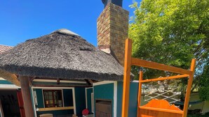 Eine Terrasse mit einem Reetdach, einem Holztisch, Stühlen, einer Holzbank und einem kleinen Tisch sowie einem Blumentopf.