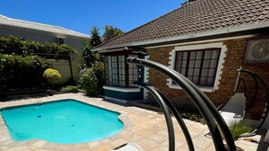 Ein Pool mit gefliestem Rand, eine Liege und ein Haus mit einem Ziegeldach und Fenstern.