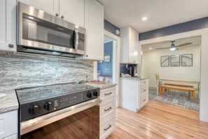 A modern kitchen with a built-in microwave, stove, and white cabinetry. There is a dining area with a bench and a ceiling fan.