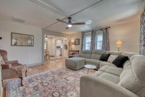 Ein Wohnzimmer mit einem großen Ecksofa, einem kleinen runden Tisch, einem gemusterten Teppich und einem Deckenventilator.