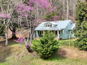 A house with a porch, surrounded by trees and a small bush.