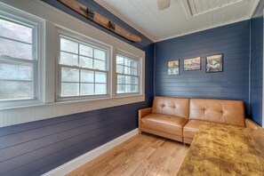 A room with a dark blue wall, a wooden floor, a leather sofa, and a window with white trim.