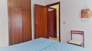 Un dormitorio con cama, armario de madera, una silla y una lámpara de pared.