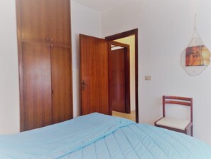 A bedroom with a bed, a wooden wardrobe, a chair, and a wall-mounted light fixture. - Spacious apartment with side sea view (Bibione)