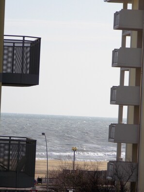 Blick auf das Meer von einem Balkon mit einem Maschengitter, einer Straßenlaterne und einem Gebäude mit Balkonen.