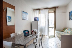 A room with a dining table, chairs, a laptop, a bed, and a TV. - Spacious apartment with side sea view (Bibione)