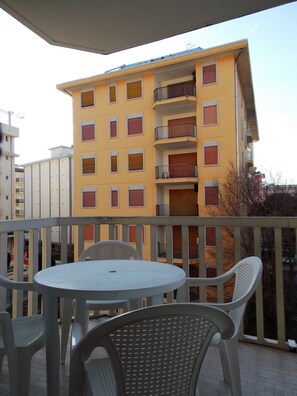 Ein Balkon mit Tisch und Stühlen, mit Blick auf ein gelbes Gebäude mit zahlreichen Fenstern und Balkonen.