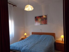 Ein Schlafzimmer mit einem Bett, zwei Nachttischen mit Lampen, einem Bild an der Wand und einem Fenster mit Vorhängen.
