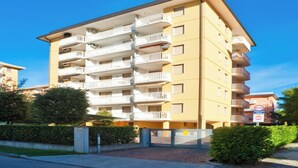 Un edificio residencial de varios pisos con balcones, una entrada protegida por un portón y un cielo despejado.