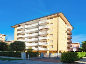 Ein mehrstöckiges Wohnhaus mit Balkonen, einem verschlossenen Eingangsbereich und blauem Himmel.