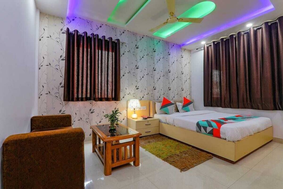 A bedroom with a bed, nightstand, lamp, curtains, and a small table with a plant.