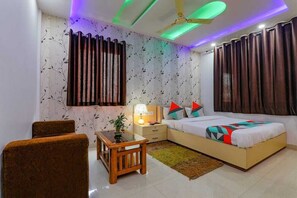 Un dormitorio con cama, mesita de noche, lámpara, cortinas y una pequeña mesa con una planta.