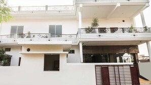 Un edificio de dos plantas con balcones, una entrada protegida por un portón y una ventana pequeña.