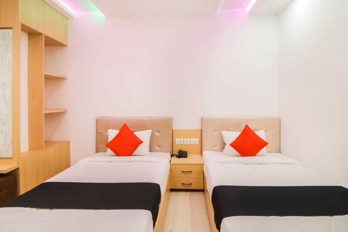 A hotel room with two beds, a nightstand, and a wall-mounted shelf.