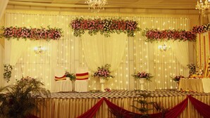 Un espacio interior con filas de asientos, un escenario con decoración floral y una araña.