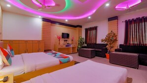 Habitación de hotel con dos camas, televisión, escritorio, sofá y ventilador de techo.
