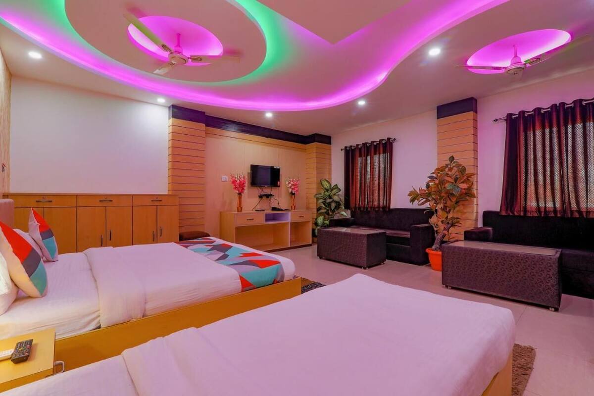 A hotel room with two beds, a TV, a desk, a sofa, and a ceiling fan.