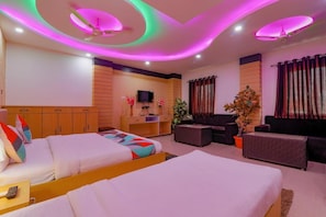 A hotel room with two beds, a TV, a desk, a sofa, and a ceiling fan. - Hotel Moti Mahal (Varanasi)