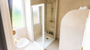 Een badkamer met een glazen douchecabine, een witte wastafel en een raam.