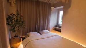 Een slaapkamer met een bed, een plant in pot en een raam.