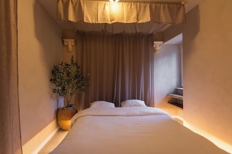 A bedroom with a bed, curtains, a plant, and a staircase.. Villa Hermès - Ancient Greece themed accommodation, near Puy du Fou