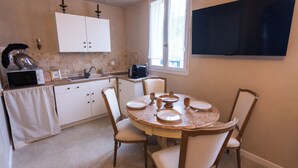 Een keuken met witte kasten, een eettafel gedekt met borden en bestek, een koffiezetapparaat en een aan de muur bevestigde televisie.