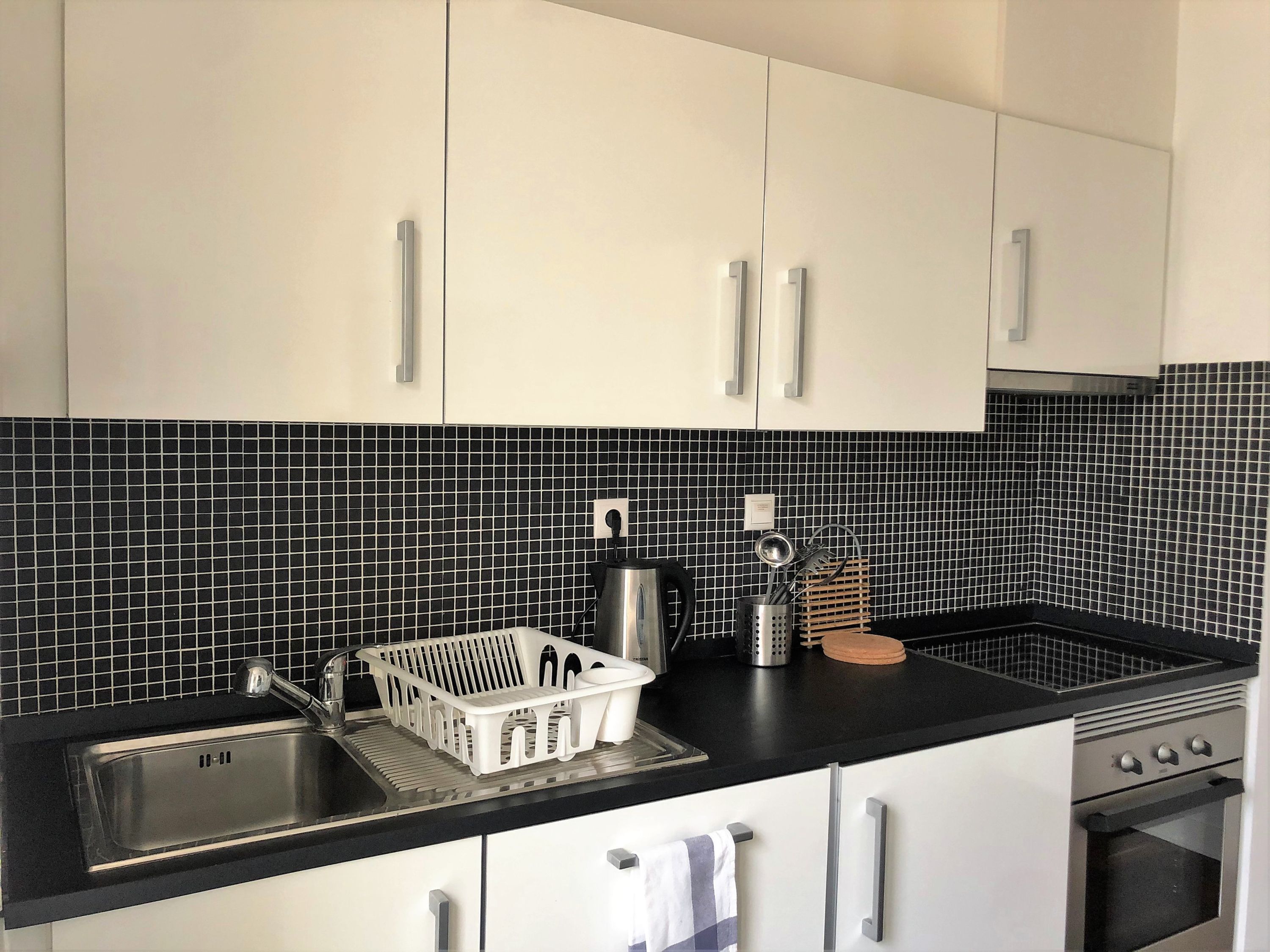 A kitchen with white cabinets, a black countertop, a stainless steel sink, and a tiled backsplash.