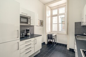 Eine Küche mit weißen Schränken, einer Mikrowelle, einer Kaffeemaschine und einem Fenster mit Jalousien.