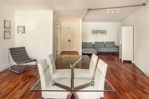 Ein zeitgemäßer Wohnraum mit Esstisch aus Glas, einem grauen Sofa, einem weißen Couche und einem weißen Schrank.