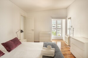 A hotel room with a bed, a bedside table with a lamp, a dresser, and a view of the outside. - Downtown Riverside V by Homing (Lisbon)
