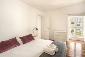 Ein Schlafzimmer mit Bett, Kissen, einem Nachttisch mit Lampe, einem Schminktisch und einem Fenster mit Blick.