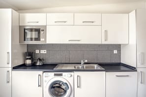 A modern kitchen with white cabinets, a microwave, a coffee maker, and a washing machine. - Downtown Riverside V by Homing (Lisbon)