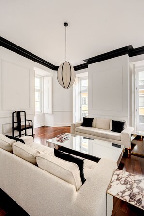 A modern living room with a white sofa, a black chair, a marble coffee table, and a pendant light. - Chiado Deluxe by Homing (Lisbon)