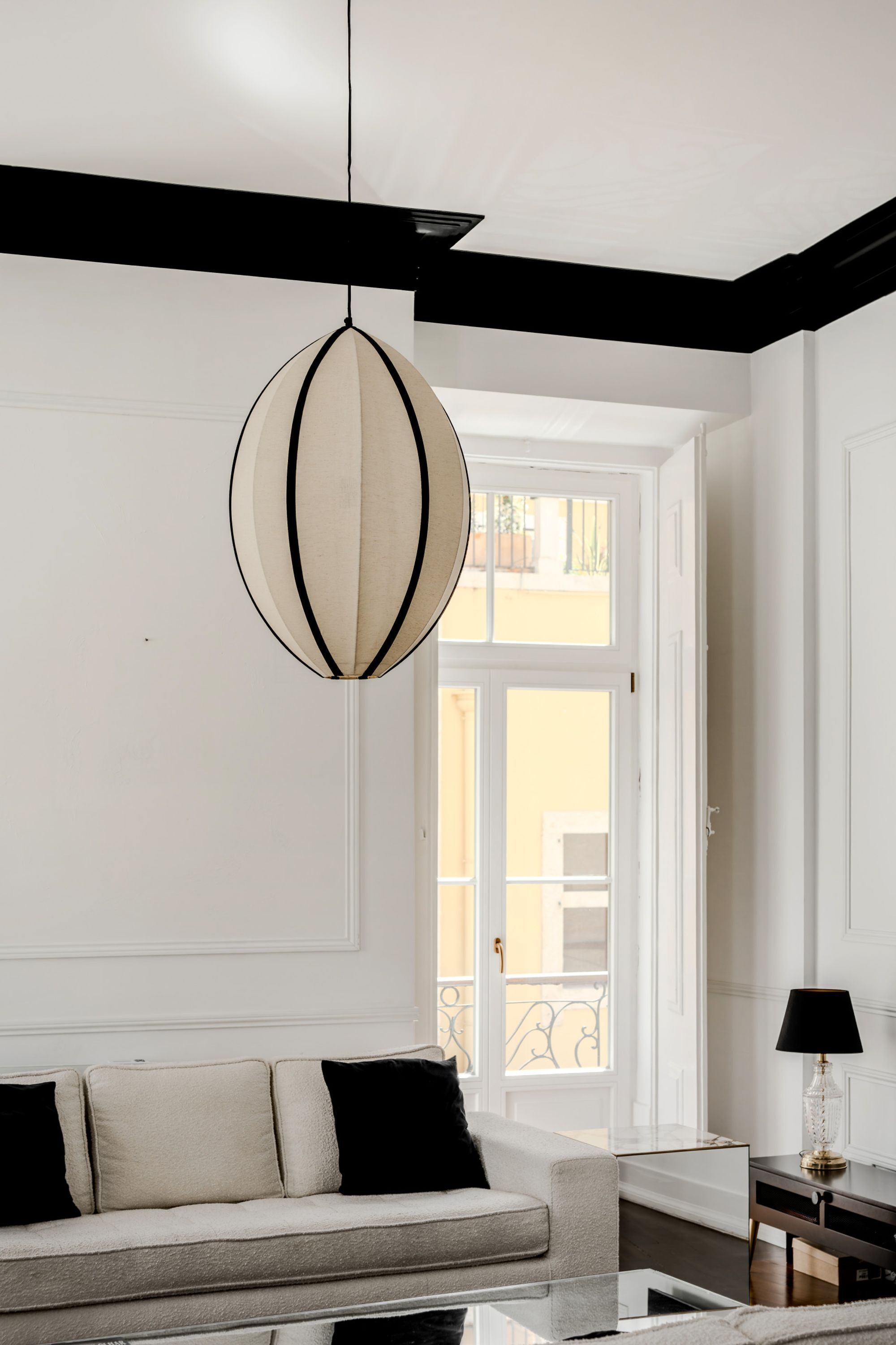 A modern living room with a sofa, a hanging light fixture, and a view of the outside.