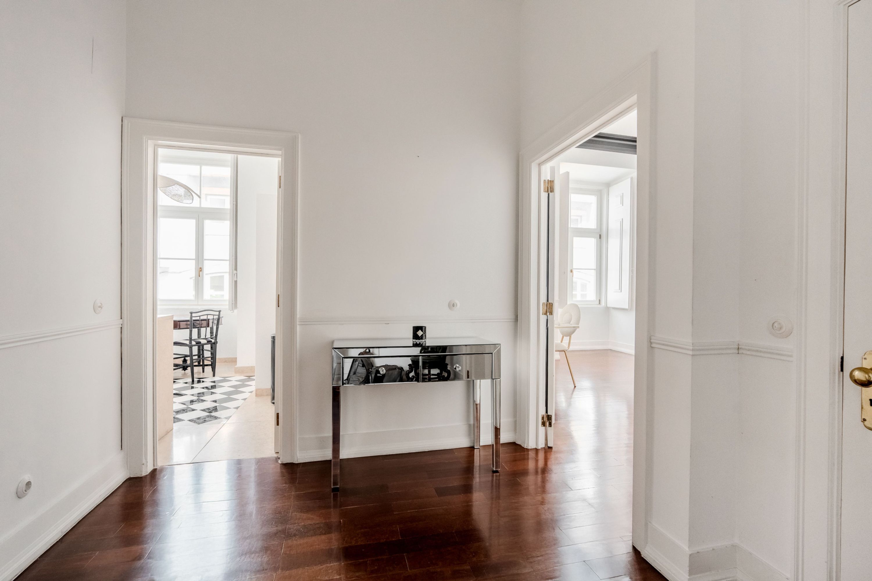 A hallway with a glass-top table, wooden flooring, and white walls.