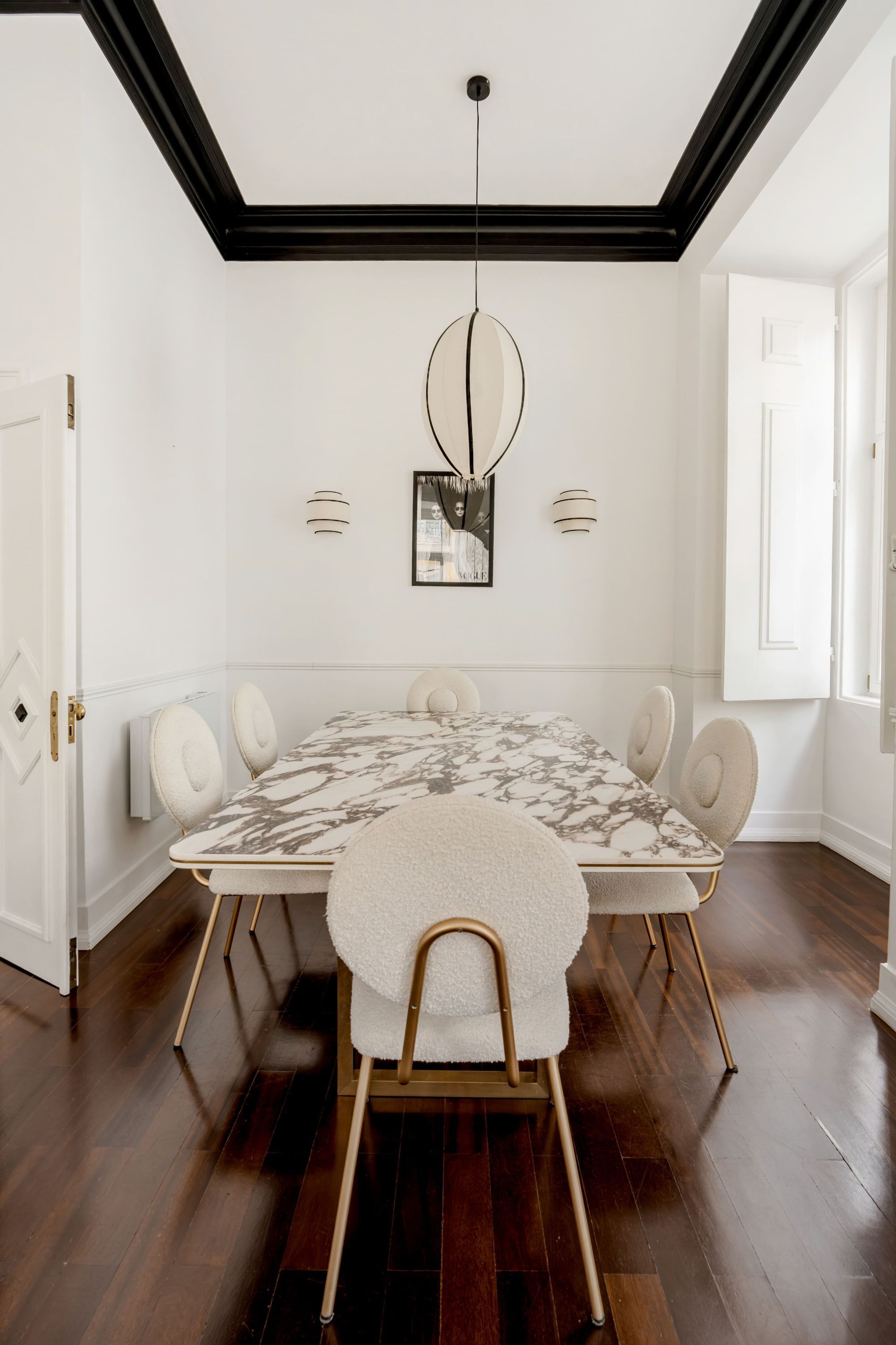 Una sala da pranzo con un tavolo in marmo, sedie imbottite bianche, un lampadario e una cornice nera a soffitto.
