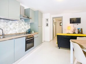 A compact kitchen with a built-in oven, a microwave, and a coffee maker. There is a dining area with a table and chairs, and a TV mounted on the wall. - La Tana by Interhome (Castiglioncello)