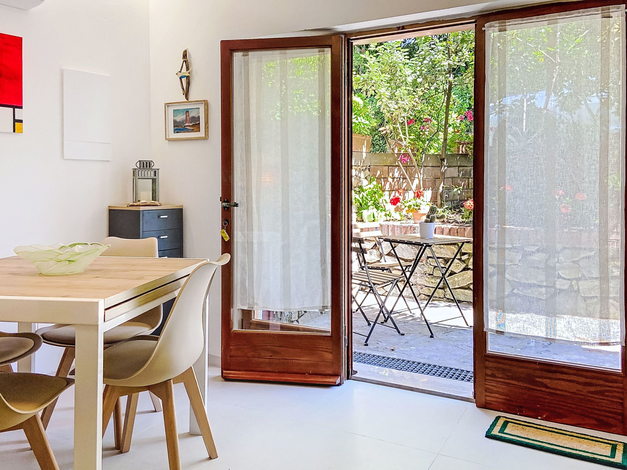 A dining area with a table and chairs, a cabinet, and a door leading to an outdoor patio with a garden view.