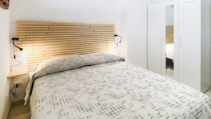 A bedroom with a wooden slat headboard, a patterned bedspread, a bedside lamp, an air conditioning unit, and a wardrobe. - La Tana by Interhome (Castiglioncello)