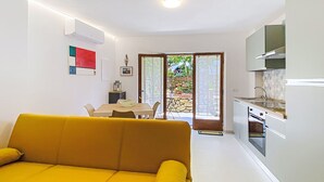 A modern living room with a sofa, a dining area with a table and chairs, a kitchen with a stove and cabinets, and a sliding glass door leading to an outdoor area. - La Tana by Interhome (Castiglioncello)